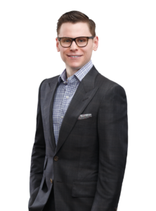 A portrait of Hunter Scott, Executive Vice President at Scott Land & Lease Ltd. He is wearing glasses and a dark suit with a checkered shirt, smiling and looking directly at the camera. The background is plain white, highlighting his professional appearance.