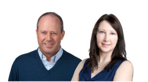 A portrait of Scott Land & Lease staff Melanie Lusk, Indigenous Administration and Communications Manager, and Donald Wilkinson, Indigenous Relations Manager. They are standing side by side against a white background. Donald on the left is wearing a blue sweater over a checkered shirt and has short hair, smiling. Melanie on the right has long dark hair and is wearing a sleeveless navy blue top, also smiling. Both are looking directly at the camera, conveying a sense of professionalism and friendliness.