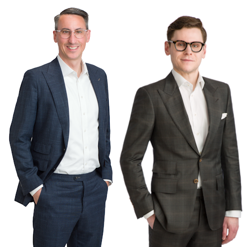 A portrait of two men from Scott Telecom Services. From left to right: Ryan Scott, President, wearing glasses and a dark suit with a white shirt, smiling with his hands in his pockets; and Hunter Scott, Executive Vice President, wearing glasses and a dark suit with a checkered shirt, smiling with his hands in his pockets. Both are standing against a white background, conveying a sense of professionalism and confidence.